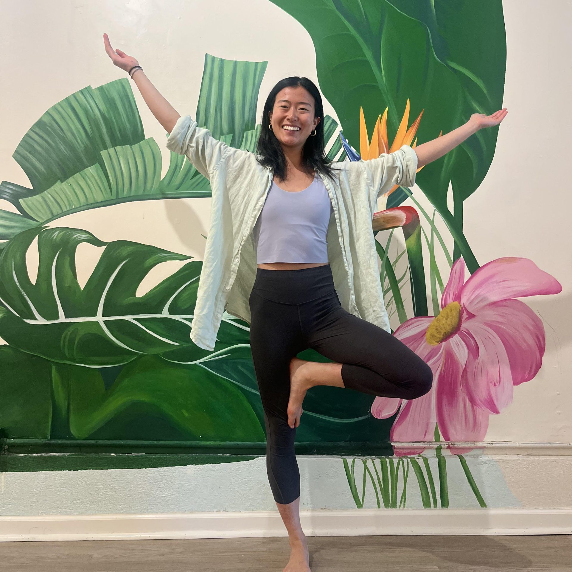 Julia in tree pose in front of a tropical mural
